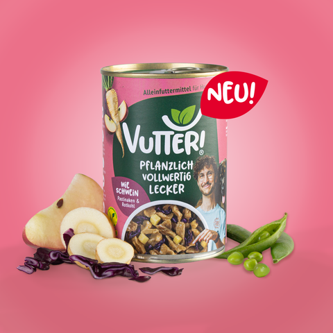 Neben einer Dose der neuen Nassfuttersorte wie Schwein in Zusammenarbeit mit Dr. Karim Montasser liegt rechts eine Sojaschote und auf der linken Seite eine Apfelspalte, drei Scheiben Pastinake und etwas geschnittener Rotkohl. Oben an der Dose ist ein rotes Schild mit dem Schriftzug Neu!