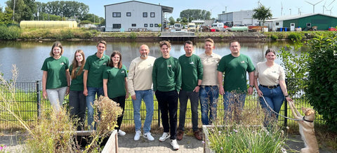 Das Vutter!-Team steht mit Vutter!-Shirts und Pullis vor einem See inklusive Bürohund Ada